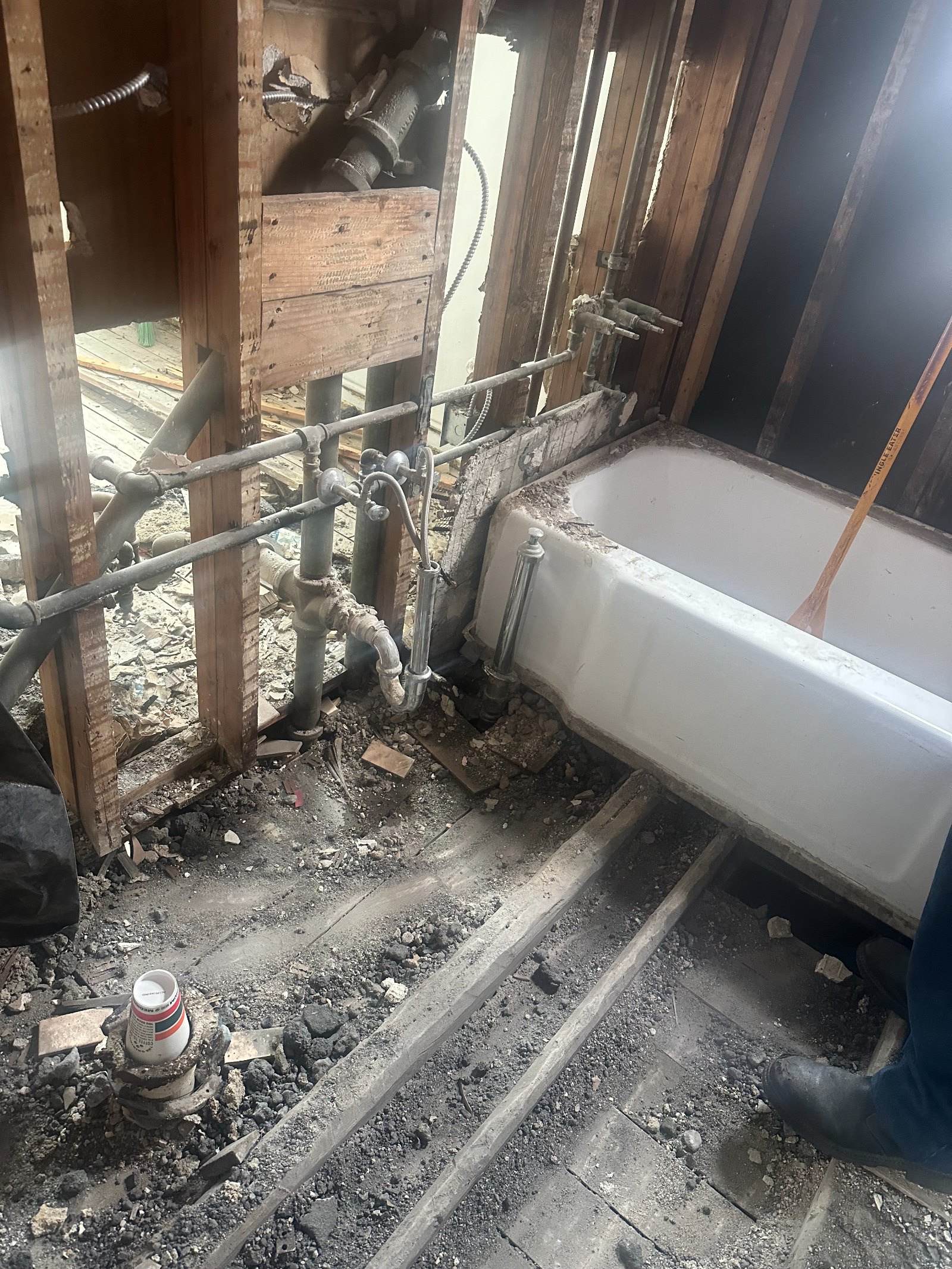 Farm equipment shed interior with white water tank, metal pipes, wooden gate, and dirt floor